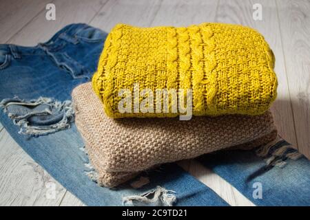 Zwei Strickpullover auf zerrissenen Jeans, ein Holzhintergrund. Modisches Konzept, Seitenansicht Stockfoto