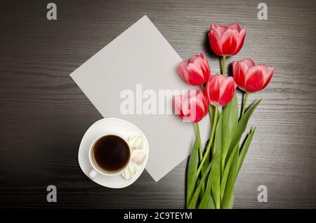 Weißes leeres Blatt Papier, rosa Tulpen und eine Tasse Kaffee. Schwarzer Tisch. Draufsicht Stockfoto