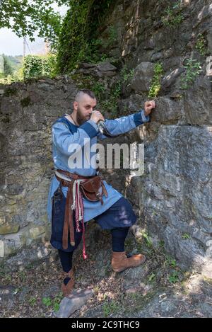 Ein Wikingerkrieger trinkt Apfelwein aus einem Horn, das an einer Steinmauer lehnt, Bild eines Mannes in mittelalterlicher Kleidung Stockfoto