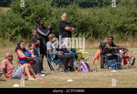 Basingstoke, Hampshire, England, Großbritannien. August 2020. Menschen, die stehen und sitzen, beobachten ein Fußballspiel für Kinder als Regeln für die Absperrung von Coronavir Stockfoto