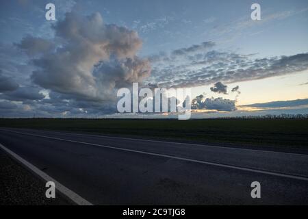 Am späten Abend leere Asphaltstraße auf dem Hintergrund der schönen Wolken bei Sonnenuntergang. Stockfoto