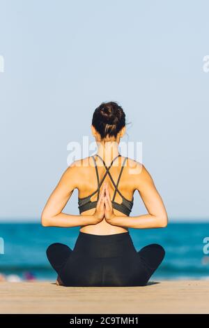 Junge Frau von hinten beim Yoga vor dem Meer an einem sonnigen Tag im Freien Stockfoto