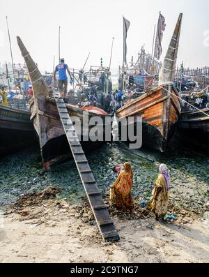 Chittagong, Bangladesch, 23. Dezember 2017: Fischer sind dabei, frischen Fang aus dem Boot zu entladen, während die einheimischen Frauen auf sie schauen Stockfoto