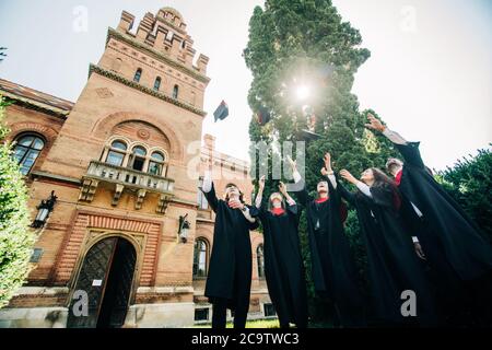 Erfolgreiche fünf Studenten mit herzlichen Glückwünschen zusammen, die Abschlussmützen in die Luft werfen und feiern. Stockfoto