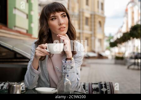 Ein Mädchen sitzt draußen in einem Café mit einer Tasse Kaffee. Junge Frau entspannt sich nach der Arbeit mit einer Tasse Kaffee Stockfoto