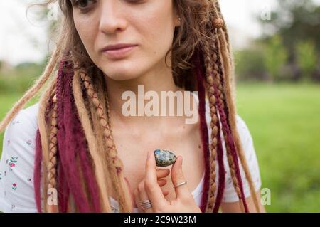 Junge schöne Mädchen mit Dreadlocks hält in der Hand Azurit, Naturstein im Freien während des Morgens in der Nähe ihres Gesichts mit perfekter Haut Stockfoto