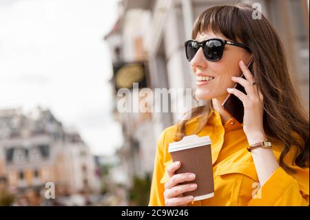 Helles Mädchen in gelbem Hemd reden am Telefon mit einer Tasse Kaffee in den Händen. Stockfoto