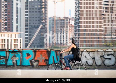 Belgrad, Serbien - 21. Juli 2020: Junge Frau, die mit dem Fahrrad über die Branko-Stadtbrücke fährt, hinter ihr die Gebäude der Balgrade Waterfront Stockfoto