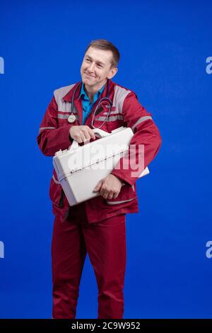 Krankenwagen Arzt Mann in einem Arbeitsanzug und mit einem Box in den Händen posiert auf einem blauen Hintergrund Stockfoto