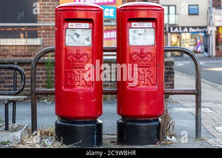 Zwei rote Royal-Briefkästen nebeneinander auf einer Straße mit einem Aufkleber mit der Angabe der Priorität Briefkasten Stockfoto
