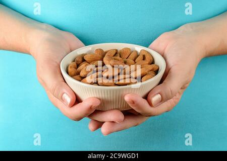 Kaukasische Frau Hände halten beige Keramik Schüssel mit rohen Mandeln. Nicht geröstete Nüsse als Antioxidans und Proteinquelle für ketogene Ernährung und Vegetarismus. Stockfoto