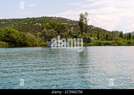 Grüne Hügel mit Wald um den Fluss Krka im schönen Nationalpark Krka, Kroatien, fahren touristische Boote entlang des Flusses Stockfoto