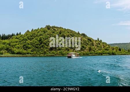 Grüne Hügel mit Wald um den Fluss Krka im schönen Nationalpark Krka, Kroatien, fahren touristische Boote entlang des Flusses Stockfoto