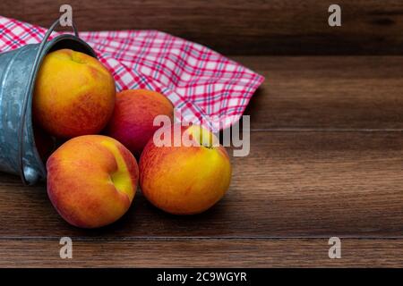 Pfirsiche in einem Eimer mit Picknick-Tischplatte auf Holzhintergrund Mit Kopierbereich Stockfoto