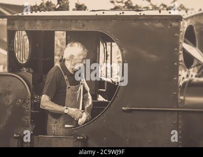 Mono close up Dampfzug Fahrer in vintage UK Dampflokomotive Kabine Vorbereitung für die Abfahrt am Heritage Bahnhof. Dampfeisenbahn Zugcrew. Stockfoto