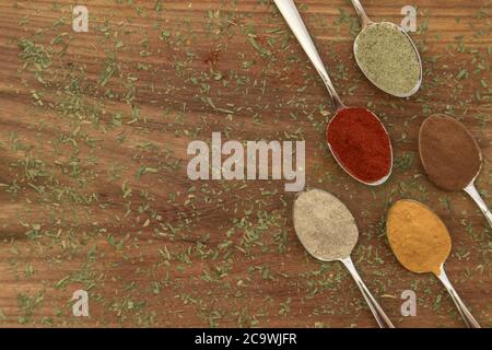 Verschiedene bunte Gewürze auf Löffeln mit Holzhintergrund angeordnet Stockfoto