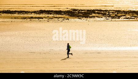 SWANSEA, WALES - OKTOBER 2018: Einzelperson, die bei Ebbe an einem leeren Strand läuft Stockfoto