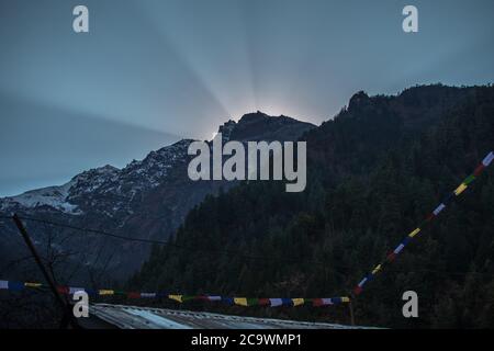 Helle Sonnenstrahlen, die auf den nepalesischen Berggipfeln über buddhistischen Gebetsfahnen auf dem Annapurna Circuit in Nepal ihren Höhepunkt erreichen Stockfoto