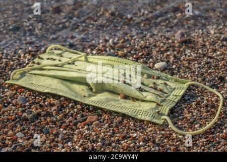 Nahaufnahme einer ausrangierten gebrauchten Gesichtsmaske liegt in der Surfzone an einem sandigen Kiesstrand. Stockfoto