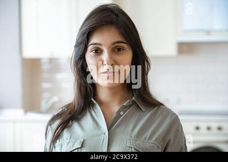 Selbstbewusste junge indische Frau, die zu Hause in der Küche die Kamera anschaut, Headshot. Stockfoto