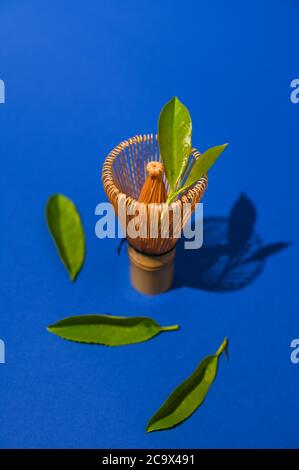 Der Teebesen passt zu frischen grünen Teeblättern. Zutaten für die Herstellung eines traditionellen japanischen Getränks. Gesundheit und alternative Medizin. Hartes Licht im Rahmen. Speicherplatz kopieren. Oben. Hochwertige Fotos Stockfoto