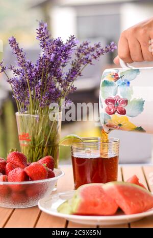 Sommerliche Erfrischung mit einem Krug, der Eistee und frisches Obst auf die Seite gießt Stockfoto