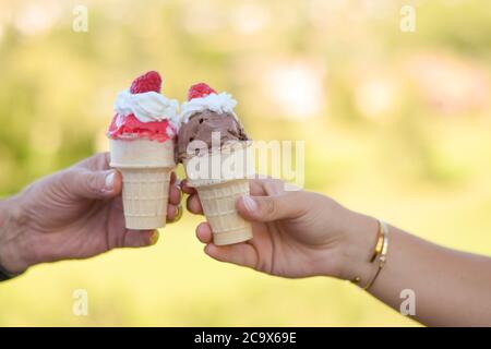 Hände mit zwei Eiszapfen mit Eis, Schlagsahne und einer Himbeere auf der Oberseite Stockfoto