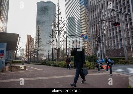 Ein japanischer Büroangestellter oder Salaryman überprüft sein Smartphone, während er in Shinjuku, Tokio, Japan, läuft Stockfoto