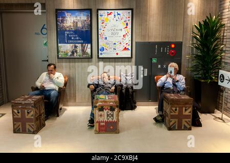 Männer sitzen und nutzen Smartphones oder schlafen beim Einkaufen im Hikarie Tower, Shibuya, Tokio, Japan. Stockfoto