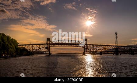 Sonnenuntergang über der Second Narrows Bridge (Ironworkers Bridge) des Trans Canada Highway und einer Eisenbahnbrücke, über Burrard Inlet und Vancouver Harbour Stockfoto