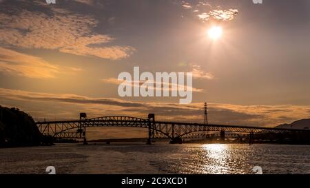 Sonnenuntergang über der Second Narrows Bridge (Ironworkers Bridge) des Trans Canada Highway und einer Eisenbahnbrücke, über Burrard Inlet und Vancouver Harbour Stockfoto