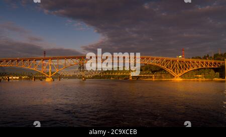 Sonnenuntergang über der Second Narrows Bridge (Ironworkers Bridge) des Trans Canada Highway und einer Eisenbahnbrücke, über Burrard Inlet und Vancouver Harbour Stockfoto