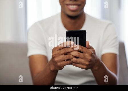 Nahaufnahme eines positiven jungen afroamerikanischen Mannes, der Textnachrichten auf seinem Smartphone liest Stockfoto