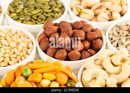 Die verschiedenen Arten von Nüssen und Samen in den weißen Keramikschalen. Stockfoto