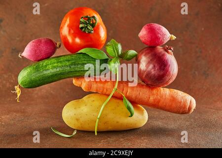 Eine Gourmet-Food-Komposition mit buntem Gemüse auf braunem Hintergrund, für eine lustige Gastronomie und vegetarisches Rezept. Gleichgewicht schwimmende Lebensmittel Balan Stockfoto