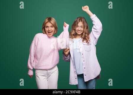 Charmante blonde Frauen posieren auf grünen Studio Wand mit den Händen über und lächeln an der Kamera Stockfoto