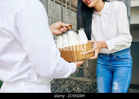 Nahaufnahme der lächelnden jungen Frau, die an den Türen ihres Hauses eine Bestellung mit frischer Milch erhält Stockfoto