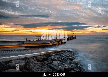 Kleiner Pier, der sich in seidig glattes Meer bei Sonnenuntergang erstreckt - lange Aussetzung Seestück Stockfoto