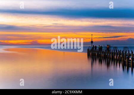 Lebhaft leuchtend orange Sonnenuntergang über Meer und Bootssteg - lange Belichtung Seestück Stockfoto