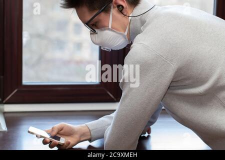 Ein junger Mann in einer medizinischen Maske nimmt ein Selfie am Telefon während der Quarantäne zu Hause Stockfoto