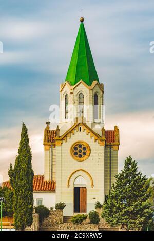 Toller Blick auf die Fassade der alten katholischen Kirche mit üppigem Garten vor dem Hintergrund des bunten Himmels während des Sonnenuntergangs Stockfoto