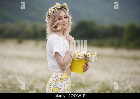 Hübsche junge blonde Frau mit Kamillen in weiß blühenden Feld. Mädchen in Kamillenkranz Stockfoto