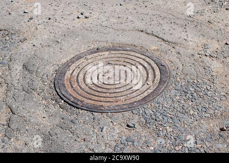 Rundschachtloch auf altem Asphalt im Sand aus nächster Nähe Stockfoto