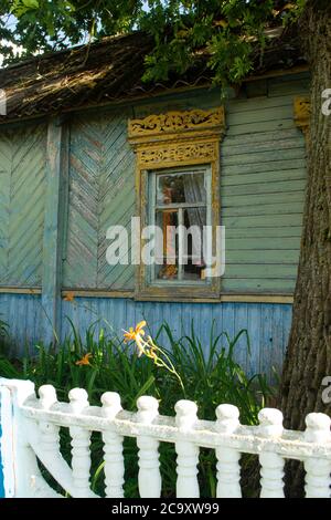 Traditionell verzierten gelben offenen Fensterläden des alten hölzernen ländlichen Hauses im Dorf Weißrussland. Altes schäbiges blaues Haus Stockfoto