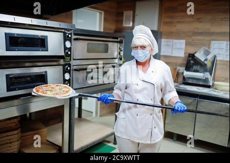 Pizzahersteller in Schutzmaske in der Pizzeria arbeiten. Stockfoto