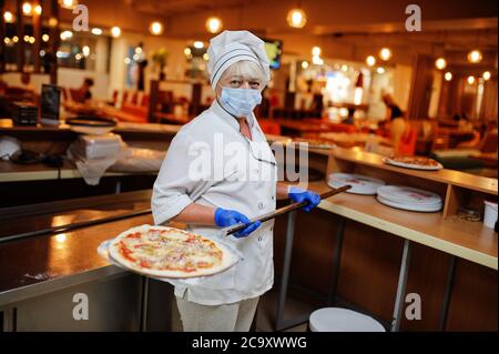 Pizzahersteller in Schutzmaske in der Pizzeria arbeiten. Stockfoto