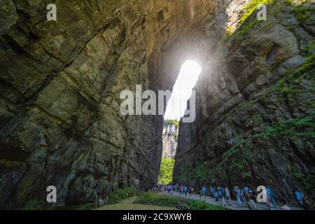 Wulong, China - August 2019 : Massen von Touristen zu Fuß auf einem schmalen Weg in Richtung der natürlichen felsigen Bogenspaltung in einer Schlucht unter Karstlandschaft Stockfoto