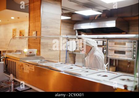 Pizzahersteller in Schutzmaske in der Pizzeria arbeiten. Stockfoto