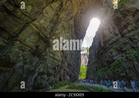 Wulong, China - August 2019 : Massen von Touristen zu Fuß auf einem schmalen Weg in Richtung der natürlichen felsigen Bogenspaltung in einer Schlucht unter Karstlandschaft Stockfoto