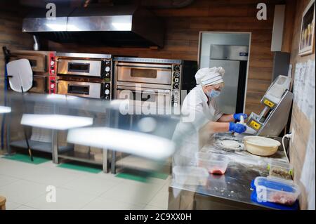 Pizzahersteller in Schutzmaske in der Pizzeria arbeiten. Stockfoto
